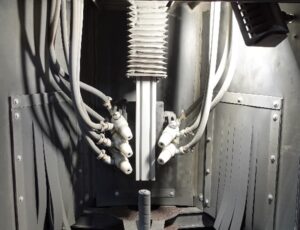Inside view of an industrial machine featuring several white hoses connected to a central vertical cylinder with metal fittings, all housed within a robust metal enclosure—an arrangement often integrated with a Rotary Indexing Table for precise, automated part positioning.