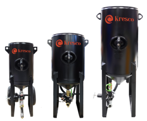 Three black industrial tanks of varying sizes, labeled Kresco in orange, are displayed side by side on a white background. Each tank, ideal for use as a Media Storage Hopper or with Pressure Blasters, features a top handle and metal legs or wheels for support.