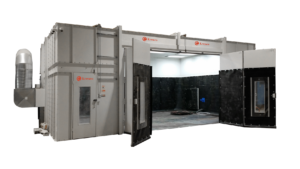 Large industrial Blast Booth Enclosure with open double doors, white exterior, ventilation system on the left, and black interior walls. Some cables and equipment are seen on the floor inside the booth.