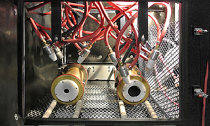 Close-up view of automation-ready sandblast cabinets featuring multiple red cables connected to cylindrical metal components, all arranged on a metal grid platform inside an enclosed chamber.