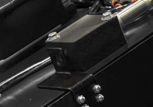 Close-up of a black metal machine part with bolts, showing a rectangular component attached to a flat metal base, and cables in the background—part of the secure blasting cabinet door for enhanced safety.