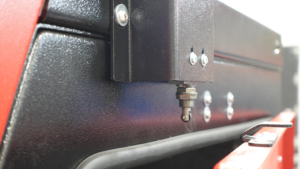Close-up of a metal latch mechanism on a red and black blasting cabinet door, possibly part of industrial equipment, with bolts and a rubber seal visible.